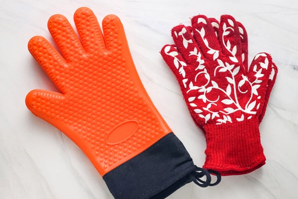 Orange silicone mitts and red oven gloves on a table.