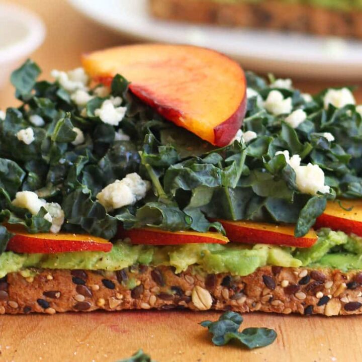 Closeup of toasted bread topped with peach slices, avocado, greens, and crumbled gorgonzola cheese.