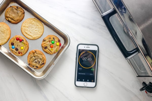 Timer screen on a cell phone next to a toaster oven and sheet pan of cookies.