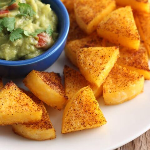 Smoky baked polenta triangles with a small bowl of guacamole.
