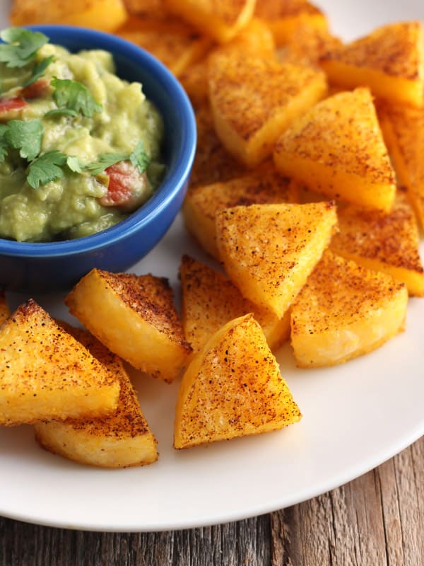 Seasoned polenta triangles on a white plate with a small blue bowl of guacamole.