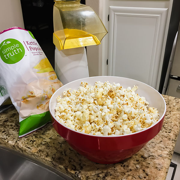 A red bowl full of popcorn, bag of kettle corn and popcorn air popper on a kitchen counter.