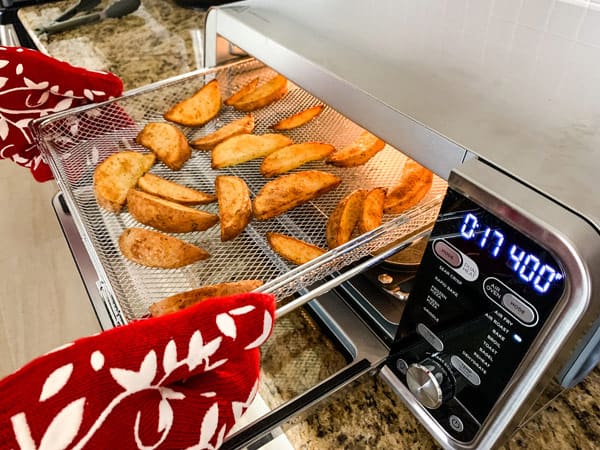 Person pulling basket of potato wedges out of an air fryer toaster oven.