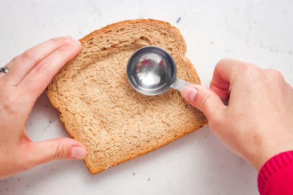 Hand pressing tablespoon in center of a bread slice.