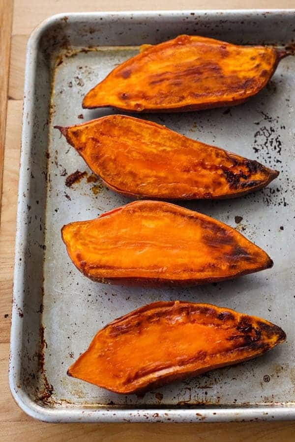 Cooked sweet potato halves on a quarter sheet pan.