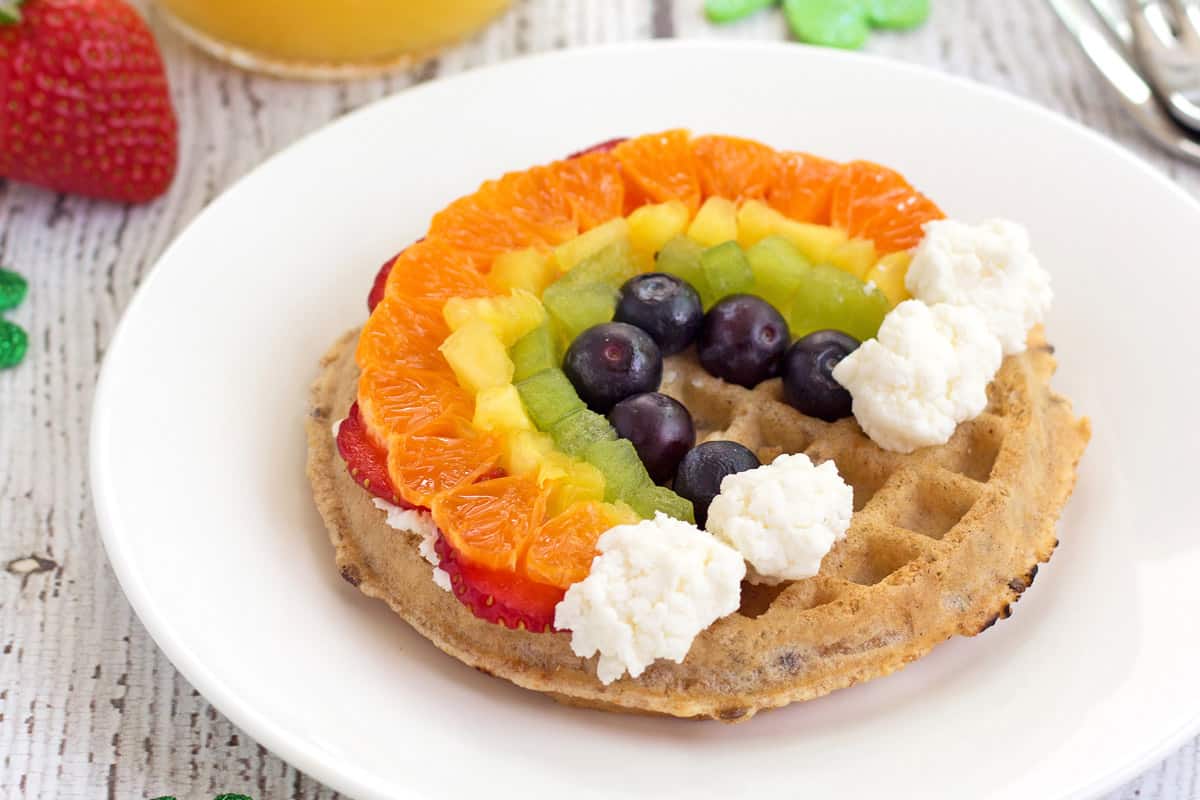 Plate with waffle topped with fruit in the shape of a rainbow.