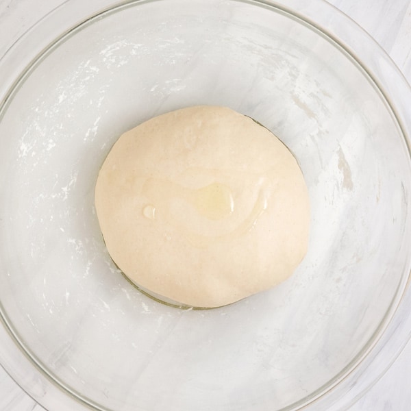 Overhead view of dough ball coated with olive oil in a dirty mixing bowl.