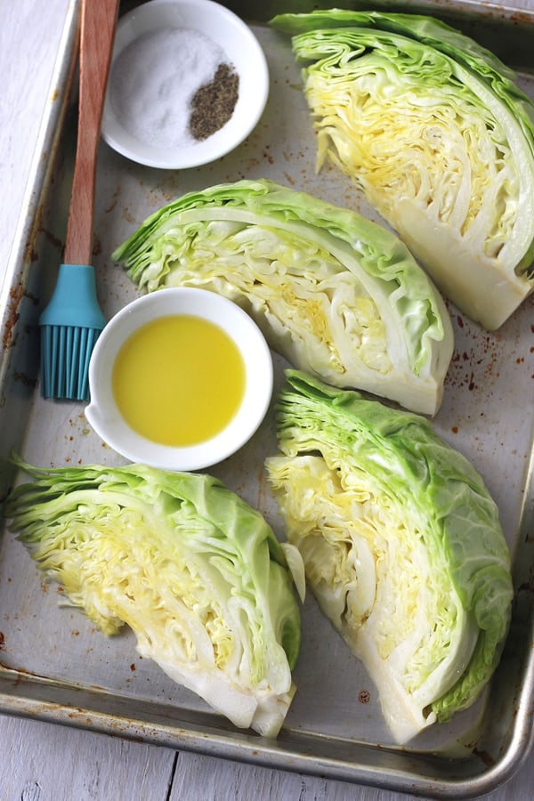 Cabbage wedges on a baking sheet with oil, salt, pepper, and a silicone brush.