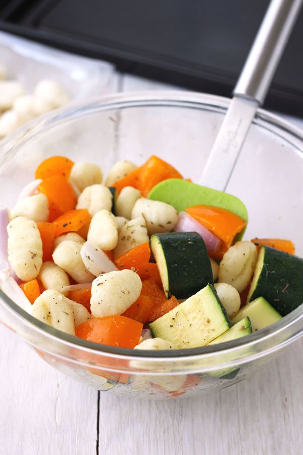 Chopped zucchini, orange bell pepper, shallots and gnocchi in a glass bowl