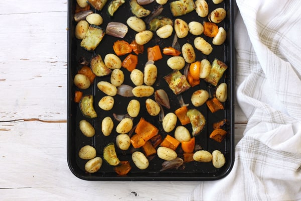 A dark roasting pan with roasted gnocchi and vegetables.