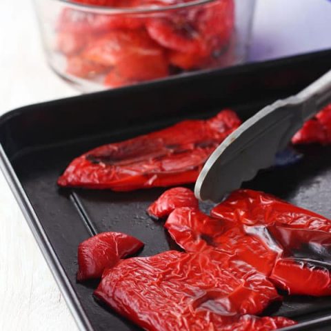 Cooked red peppers with blackened spots on a roasting pan.