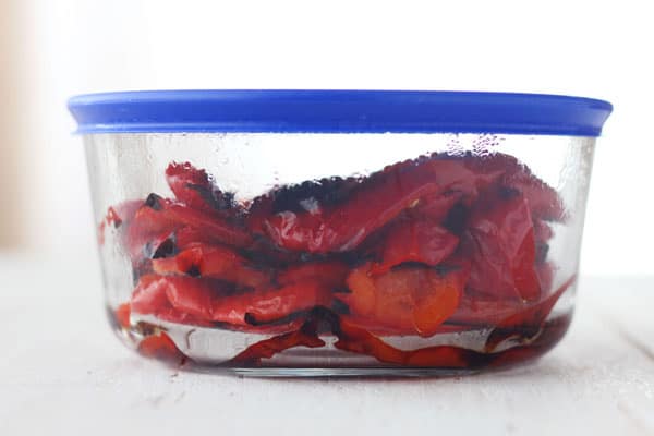 Cooked red peppers steaming in a covered container.