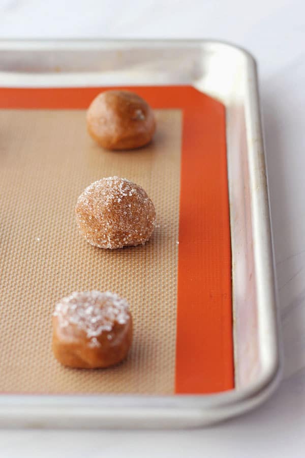 Dough balls rolled in sugar on a silicone mat lined quarter sheet pan.