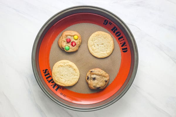 Variety of baked cookies on a baking mat in a round pan.