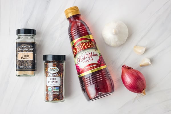 Jars of garlic powder, chili peppers, and red wine vinegar with a garlic clove and shallot.