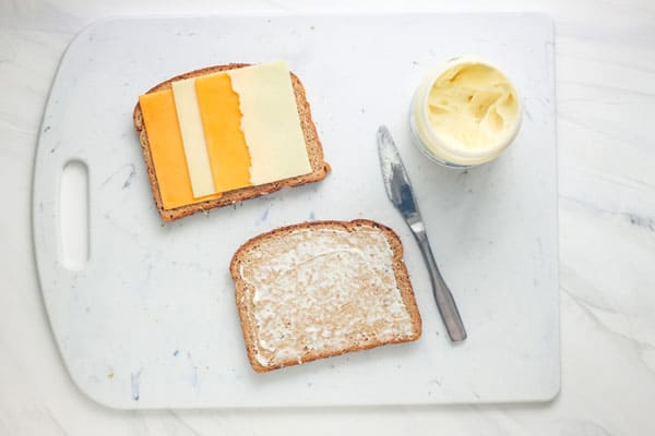 Cutting board with jar of mayo and sliced bread topped with cheese.