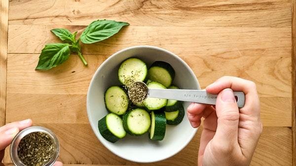 Sliced zucchini in a bowl sprinkled with Italian seasoning.