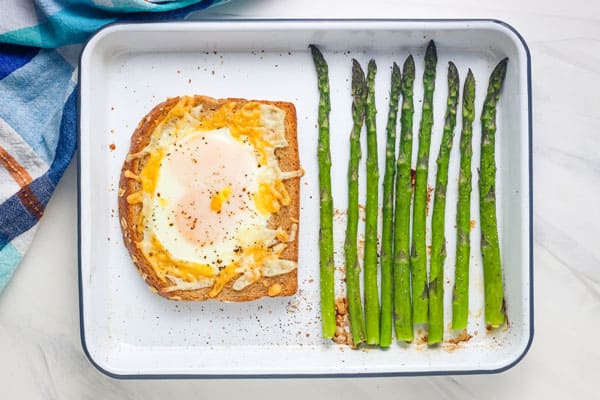 Sheet pan with roasted asparagus spears and baked egg toast.