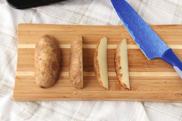 Potato sliced into wedges on a cutting board.