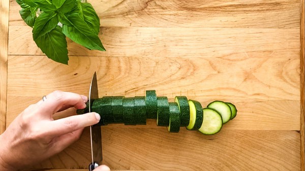 Hands slicing a zucchini into rounds on a cutting board.