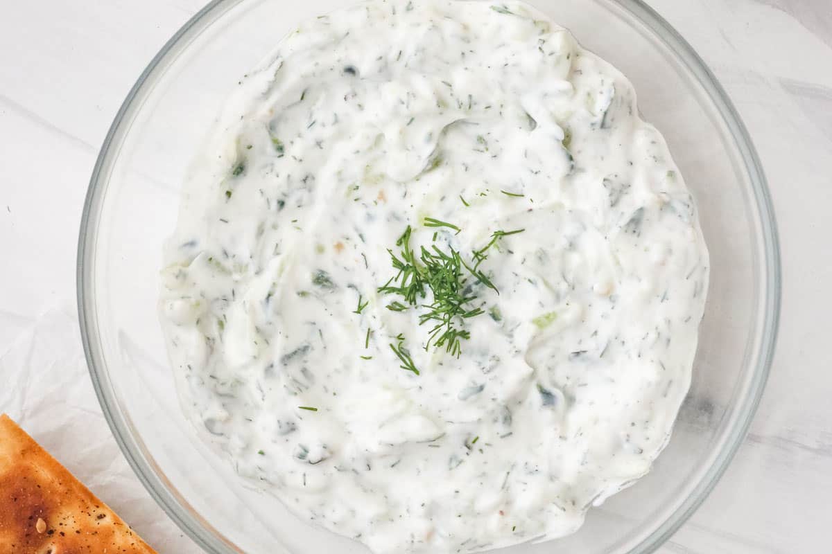 Small bowl of creamy tzatziki sauce with toasted pita chips.