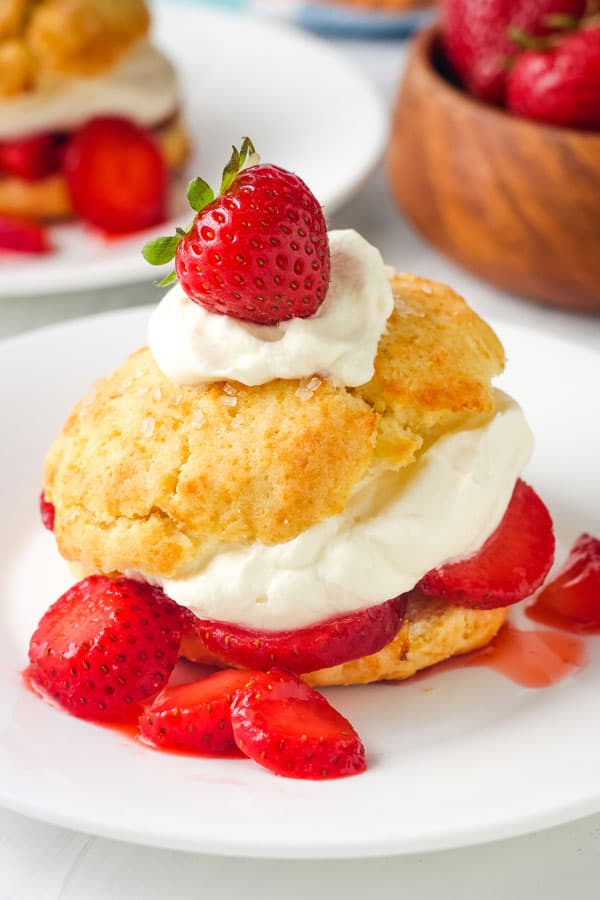 Plate with split biscuit topped with strawberry slices and whipped cream.