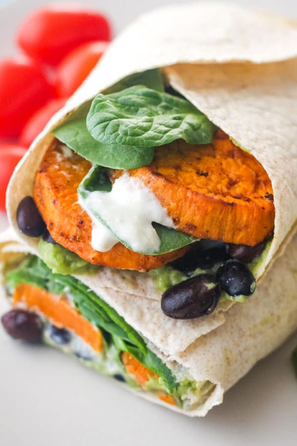 Wrap stuffed with baked sweet potatoes, spinach, beans, and sauce.