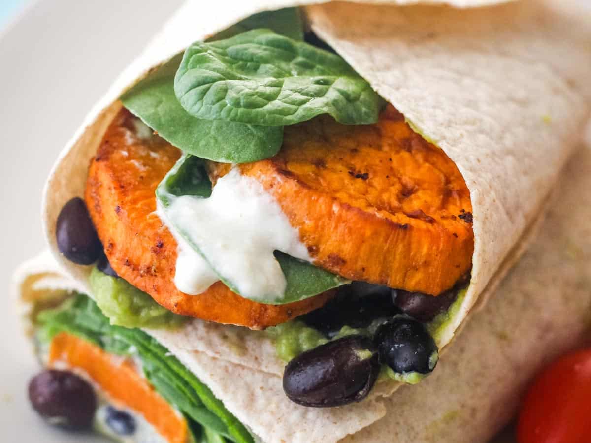 Closeup of sweet potato slices, black beans, and sauce in a wrap.