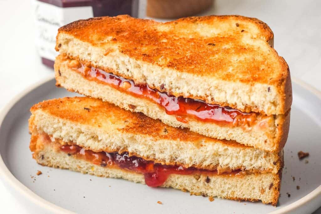 Closeup of golden toasted sandwich halves with drippy strawberry jam.