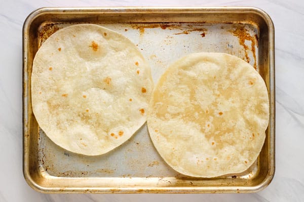 Overhead view of crisped tortillas on a sheet pan.