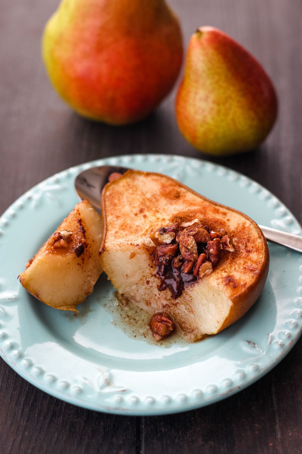 Half a baked pear on a blue plate with melted chocolate oozing out.