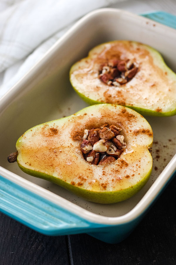 A small baking dish with two uncooked pear halves.