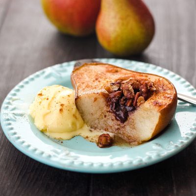 Half a baked pear on a blue plate with a scoop of vanilla ice cream.