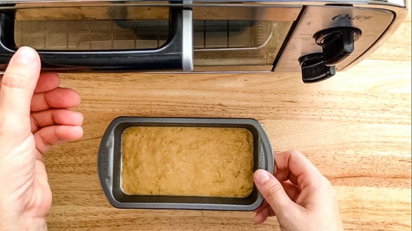 Pair of hands adding mini pan of batter to a toaster oven.