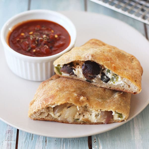 Warm toaster oven calzones on a plate with marinara sauce for dipping.