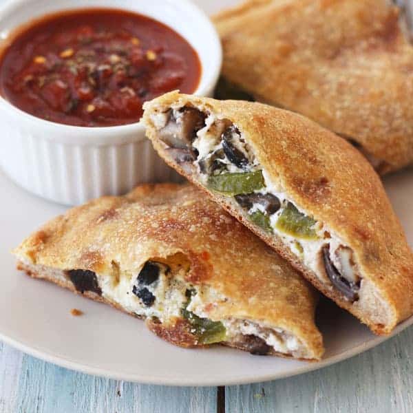 Crispy golden calzones with a side of marinara sauce on a plate.