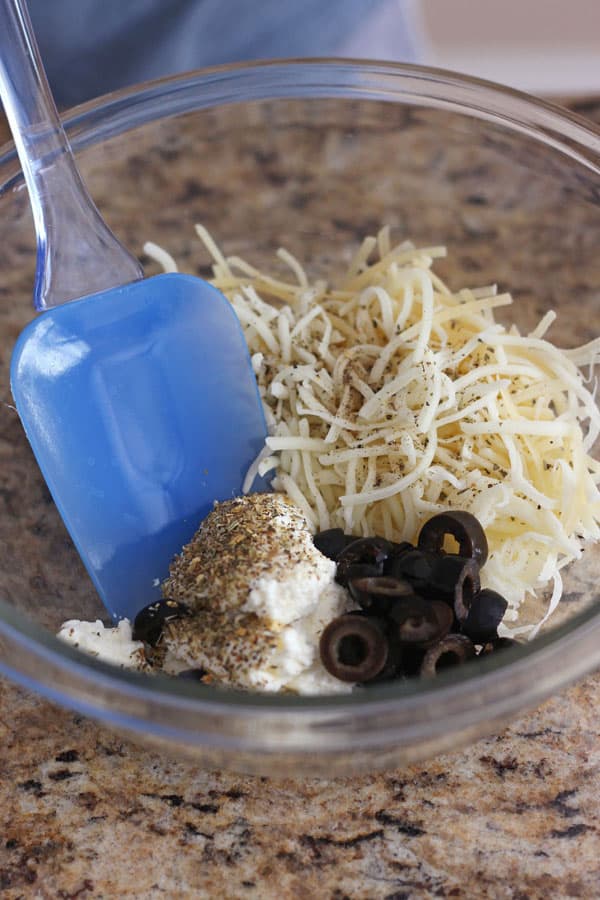 Bowl with ricotta, shredded cheese, seasoning and olives for calzones.