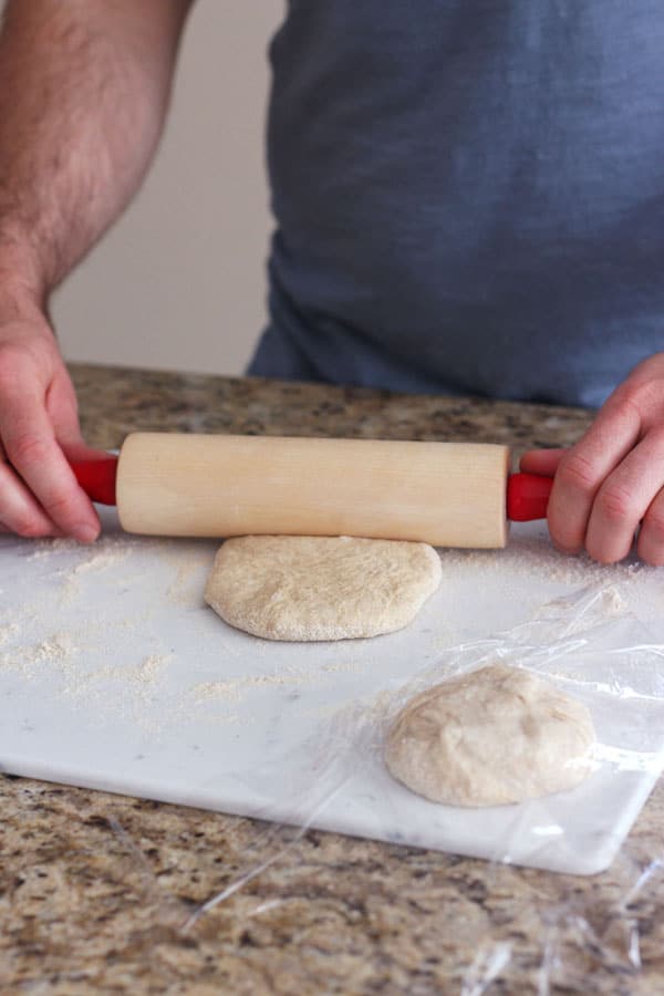 Hands rolling out a piece of dough for toaster oven calzones.