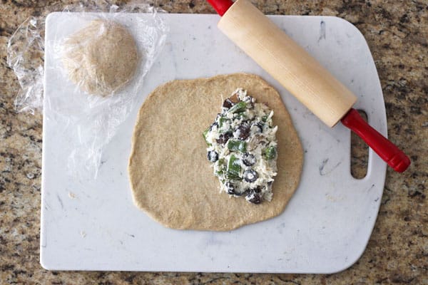 Rolled out dough with calzone filling on a cutting board.