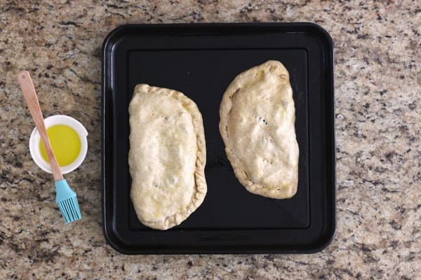 Filled calzones on a toaster oven baking pan.