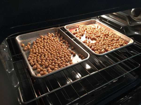 Two quarter sheet pans full of chickpeas in an oven.