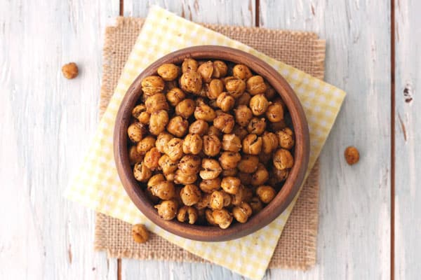 Roasted chickpeas in a wood bowl with a yellow cloth underneath.