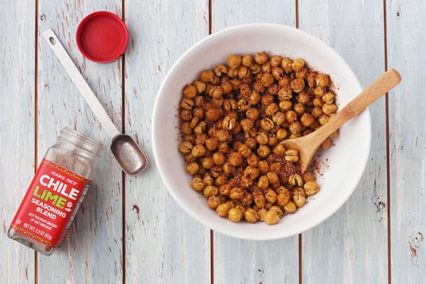 Dry roasted chickpeas in a white bowl next to a jar of chile lime seasoning.