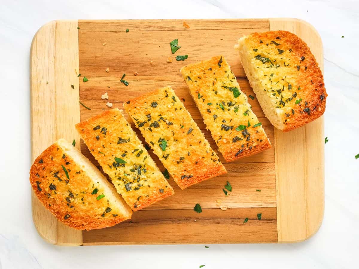 Garlic bread roll sliced into pieces on a cutting board.