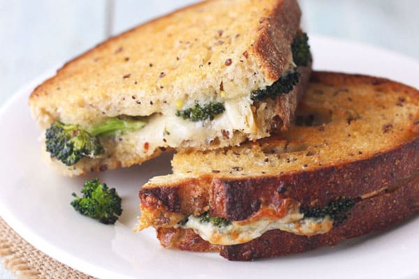 Grilled cheese with roasted broccoli inside on a white plate.