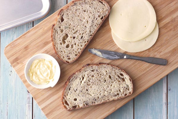 Softened butter, bread slices, and cheese on a cutting board