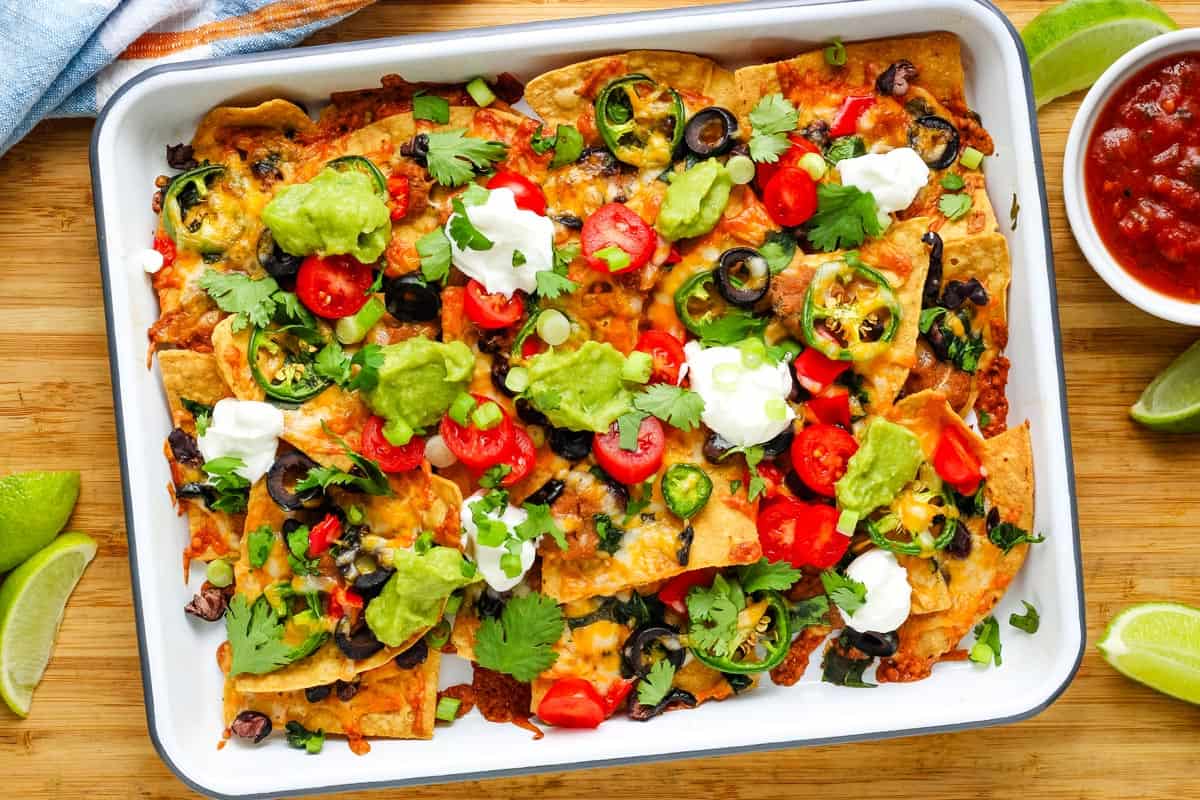 Pan of baked nachos topped with guacamole, tomatoes, green onions, and dollops of yogurt.