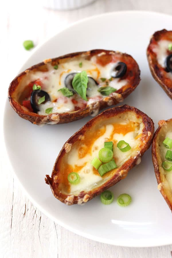 Cheesy baked potato skins on a plate topped with sliced green onions.
