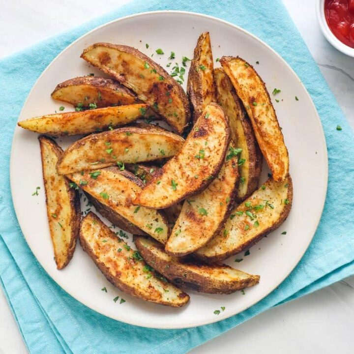 Overhead view of browned potato wedges on a white plate with ramekin of ketchup.