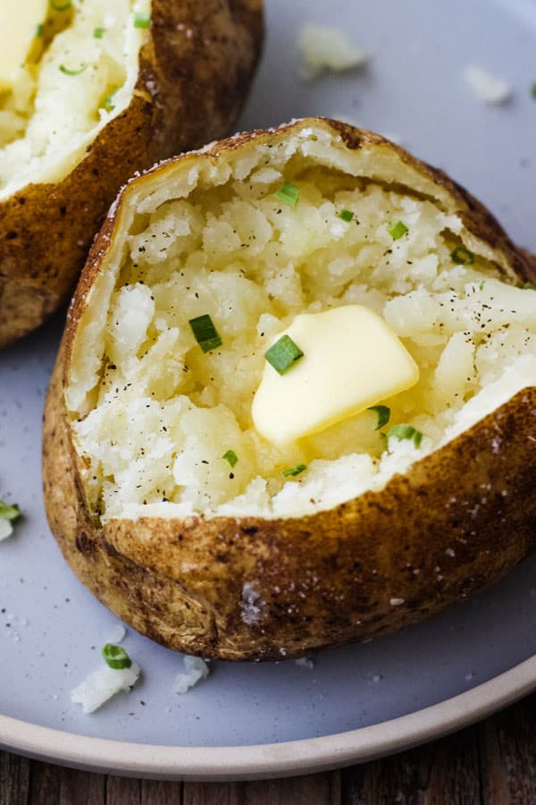 Closeup of a fluffy baked potato topped with a pat of butter and chives.